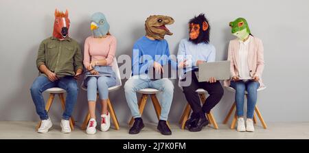 Funny people wearing animal masks sitting in waiting room, using laptops and talking Stock Photo