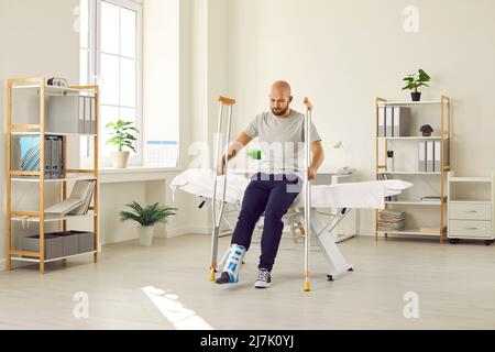 Patient with foot injury wearing support brace and trying to stand up with crutches Stock Photo