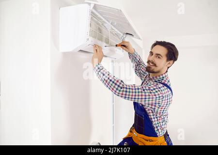 Portrait of happy young repairman using screwdriver while fixing air conditioner on wall Stock Photo