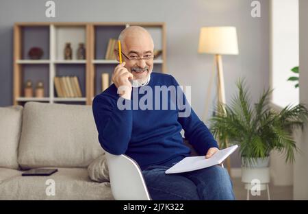 Portrait of positive elderly man who likes to write down ideas in his notebook at home. Stock Photo