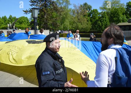 Police roll up a giant Ukrainian flag displayed by demonstrators at the Soviet War Memorial in Tiergarten, central Berlin, Germany - May 8, 2022. Stock Photo