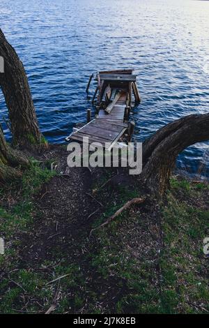 Autumn scene - lake and destroyed wooden pier. Old rotten wooden pier with missing planks with bench on a lake in the forest at autumn. Stock Photo