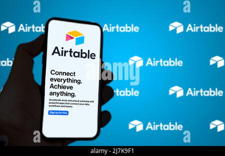 San Francisco, CA, US, May 2022: Male hand holding a phone with Airtable company web page on screen. In the background the logo Airtable blurred and r Stock Photo