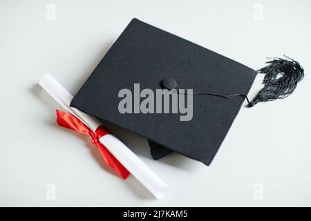 Close up of graduation cap and diploma with red ribbon on white background Stock Photo