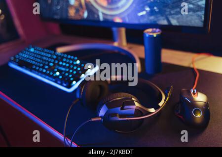 View of pro gaming desk setup with headset, keyboard, monitor and computer mouse illuminated by neon lights. Cyber sport equipment laying on desktop, ready for online video shooter games and streaming Stock Photo