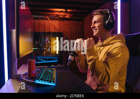Winner pro gamer celebrating his victory. Guy cyber sportsman streaming while playing shooter video games at home, feels happy with victory in online cyber sport tournament. Neon color. Side view. Stock Photo