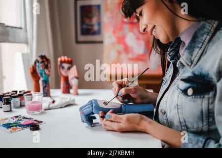 Young artist painting wood hand art pieces inside art studio indoors - Focus on hand holding brush Stock Photo