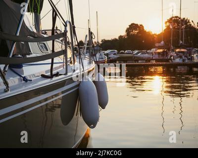 sunset view on sailing yacht moored on jetty in the port, close up view on sailboat hull, bow and fenders Stock Photo