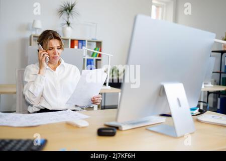Woman accountant indignantly looks at documents and talks on the smartphone Stock Photo