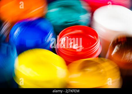 full-frame close-up background of opened small gouache paint jars with natural motion blur around red jar. Stock Photo