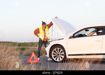 Angry man checking his broken car engine to fix it for going back home after a long trip day at work Stock Photo