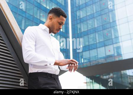Side view of serious African American male entrepreneur in formal outfit checking time while standing near multistory modern office building Stock Photo