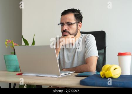 Positive beautiful female with curly hair wearing gray casual clothes sitting in light room and looking at camera Stock Photo