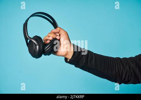 Hand of crop anonymous man holding black headphones while standing on blue background in light studio Stock Photo