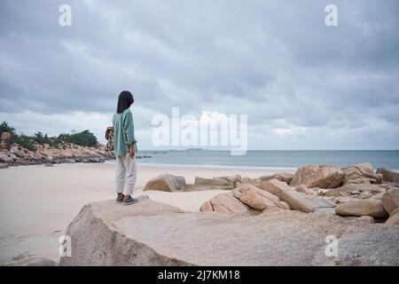 Happy young ethnic lady with long dark hair in stylish outfit standing playing with balloon against yellow background Stock Photo
