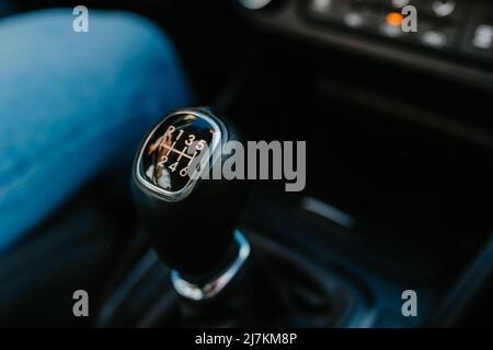 Crop anonymous driver in jeans sitting near black six speed manual shift car gear lever in automobile with dashboard during ride Stock Photo