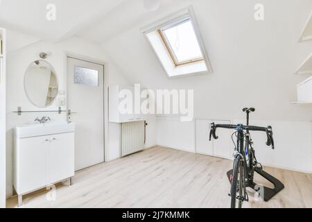 Ceramic sink on white cabinet placed at wall with round mirror in light room with black sportive bicycle at home Stock Photo
