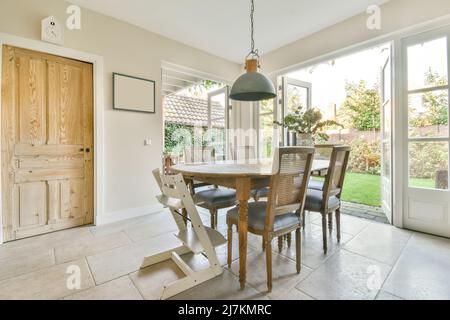 Chairs at wooden table placed in light spacious dining room in modern apartment with opened doors overlooking terrace with lawn Stock Photo