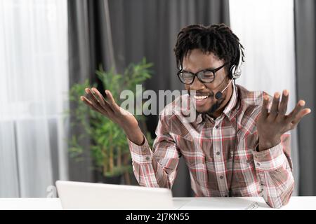 Gesturing african american freelancer looking at laptop with headphones having a group video call working distantly at home. Young student on distant leaning have a video group call.  Stock Photo