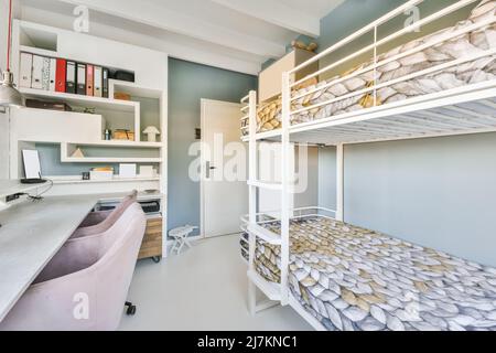 White bunk bed with soft mattresses in spacious teen room with chairs at working table with computer placed near window in daylight in modern apartmen Stock Photo