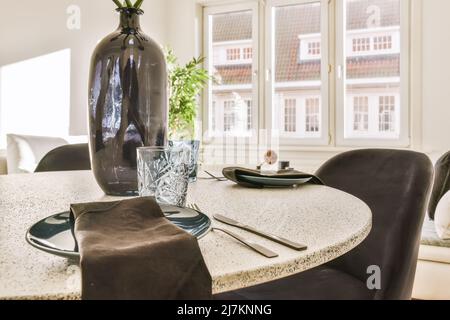 Chairs at table with vase and dinnerware placed near glass windows in light stylish dining room at home Stock Photo