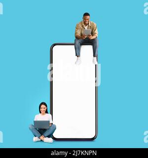 Couple sitting on white empty smartphone screen and using gadgets Stock Photo