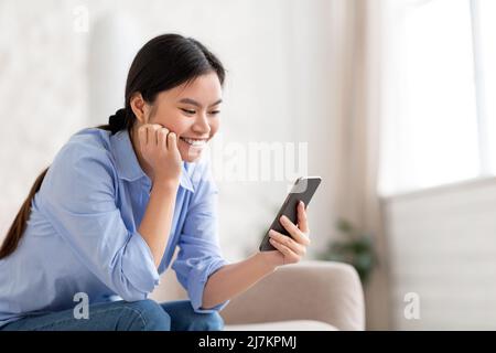 Happy chinese lady using mobile phone at home Stock Photo