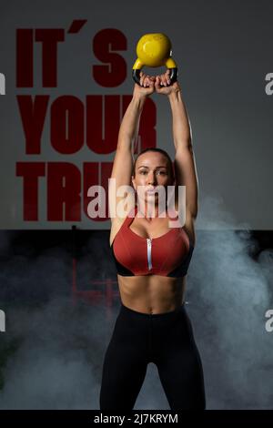 Determined young muscular female athlete in activewear doing swings exercise with kettlebell during workout in modern sports club Stock Photo