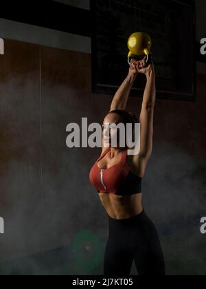 Determined young muscular female athlete in activewear doing swings exercise with kettlebell during workout in modern sports club Stock Photo