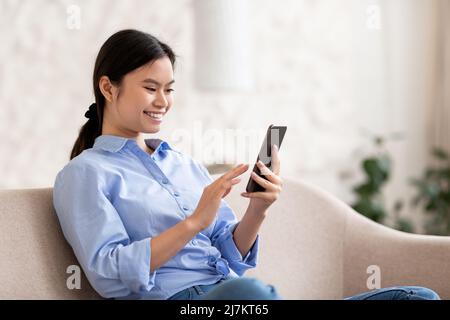 Relaxed japanese woman chilling at home, using smartphone Stock Photo