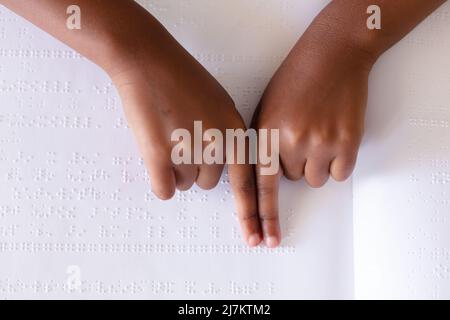 Cropped hands of african american elementary schoolgirl studying while touching braille book. unaltered, education, learning, studying, blindness, dis Stock Photo