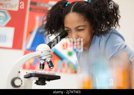 Biracial elementary schoolgirl looking through microscope during science practical class. unaltered, education, learning, scientific experiment, stem Stock Photo