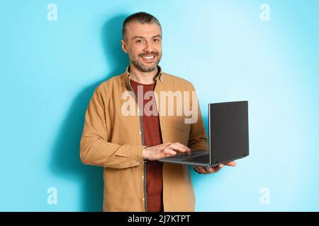 Middle Aged Freelancer Man Using Laptop Working Online, Blue Background Stock Photo