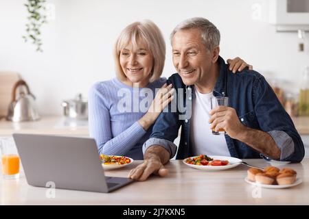 Happy senior couple using computer while having breakfast Stock Photo