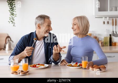 Happy elderly man and woman having lunch at home, chatting Stock Photo