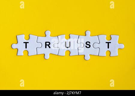 Word trust missing jigsaw puzzle on yellow cover background. Trust concept Stock Photo