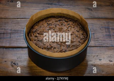Low key shot of a freshly baked fruit cake cooling in its tin, on a wooden work surface. Stock Photo