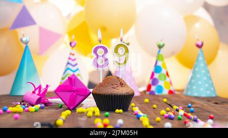 Happy birthday with candles on a background of balloons. A festive muffin with lit candles and a pink gift box for a girl. Happy birthday girl Stock Photo