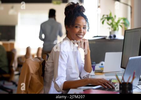 Portrait of african american mid adult businesswoman using laptop while sitting with hand on chin Stock Photo