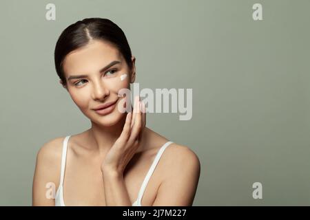 Closeup head shot pleasant beautiful woman applying moisturizing creme on face after shower. Smiling young pretty lady, daily morning routine concept. Stock Photo