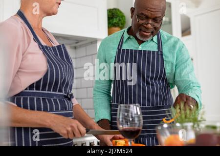 Multiracial senior couple wearing aprons preparing food in kitchen at home. unaltered, lifestyle, retirement, domestic life, cooking, food, preparatio Stock Photo