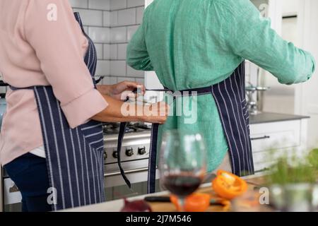 Midsection of multiracial senior couple wearing aprons while standing in kitchen at home. unaltered, lifestyle, retirement, domestic life, cooking, fo Stock Photo