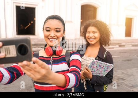 Two Latin students, a mestizo and a Hispanic taking a selfie with their cell phone outside the tourist destination of the cathedral in Leon Stock Photo