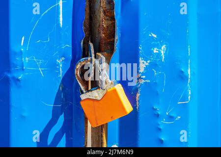 Old orange padlock on a blue metal gate Stock Photo