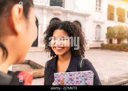 Two university students, one from the back and the other from the front, smiling with their eyes almost closed outside a university in Leon Stock Photo