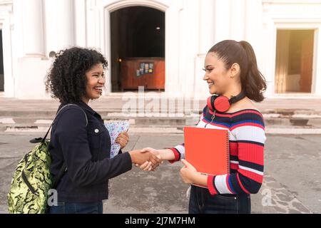 Two Latin students, one mestizo and one Hispanic shaking hands to work together and team up in their class activities. Stock Photo