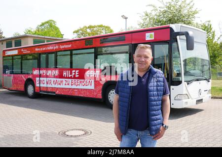 10 May 2022, Brandenburg, Neuruppin: Grigorij Koch, a Ukrainian living in Neuruppin, stands on the (OPR) stands on the depot of the Ostprignitz-Ruppiner Personennahverkehrsgesellschaft (ORP) in front of the former Corona vaccination bus of the district, which, in addition to the fresh red and white paint job, bears the lettering 'When it comes to help, we're almost unstoppable' and has been converted into a relief goods transporter. Equipped with medical equipment and medicines, the bus is to be driven to the Ukrainian crisis area in Cherkassi and then to Kharkiv. Gregorij has already organize Stock Photo