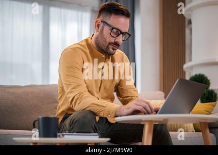 Busy adult man, reading the mail he got, while sitting on sofa at home. Stock Photo