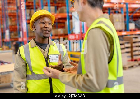 African american young male worker wearing hardhat gesturing while talking with asian mature man Stock Photo