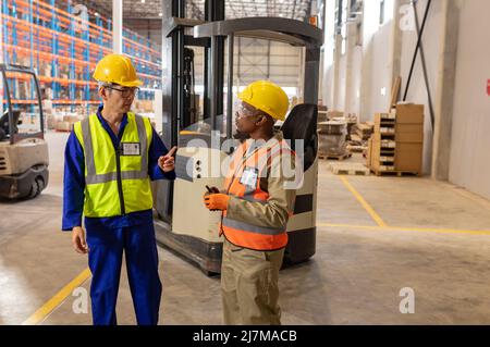 Asian mature male worker discussing with african american young man while working in warehouse Stock Photo